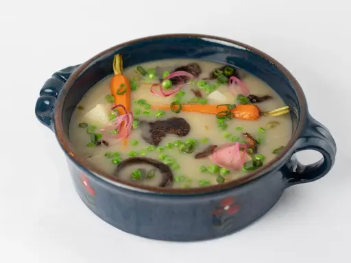 Délicieuse recette végétarienne : un potage crémeux aux carottes, petits pois, pommes de terre et champignons, garni d'oignons rouges et de ciboule.