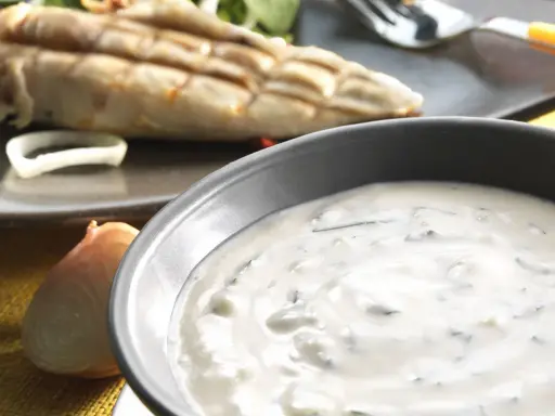 Sauce blanche crémeuse avec herbes, peut-être une différence sauce tartare et béarnaise. Poisson grillé en arrière-plan.