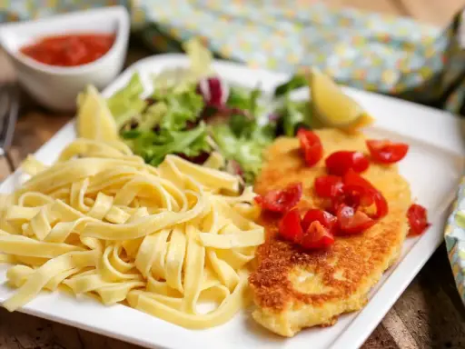 Une assiette de pâtes fraîches, une escalope milanaise dorée garnie de tomates cerises, et une salade verte. Un délice !