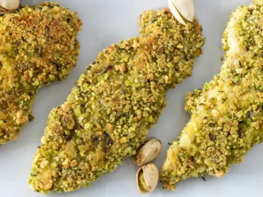 Trois tendres morceaux de poulet pistache, croustillants et dorés, sont présentés sur fond blanc.