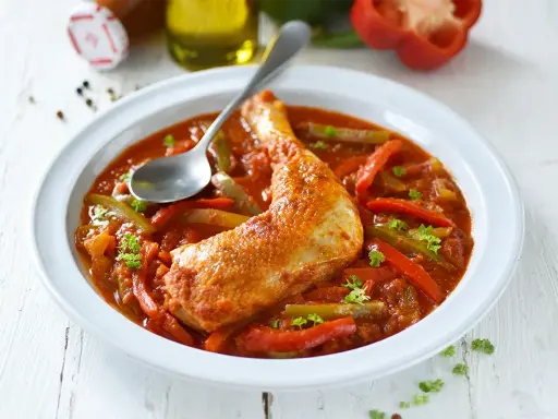 Un plat de poulet basquaise savoureux, avec un morceau de poulet doré dans une sauce tomate riche aux poivrons rouges et verts, garni de persil frais.