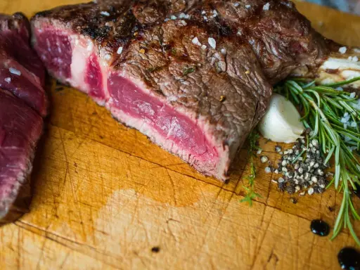 Un succulent côte de bœuf barbecue, saignant et parsemé de gros sel, est prêt à être dégusté. Accompagné de romarin frais, d'ail et de poivre concassé.