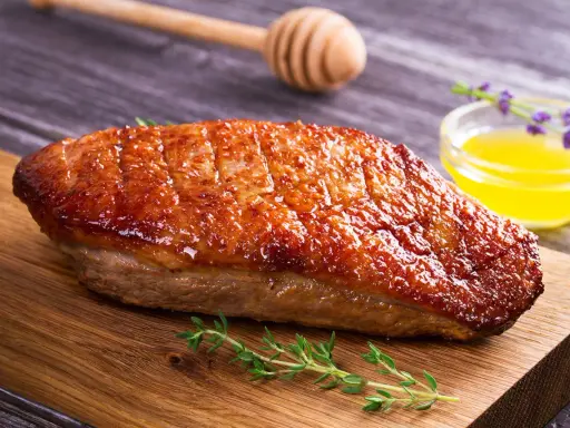 Un magret de canard au barbecue, la peau dorée et croustillante, servi sur une planche en bois avec du thym frais et une sauce au miel.