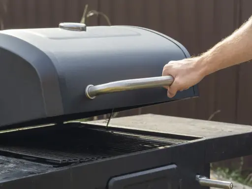 Main d'homme ouvrant le couvercle d'un barbecue noir. Apprenez comment utiliser un barbecue avec couvercle pour des grillades parfaites.