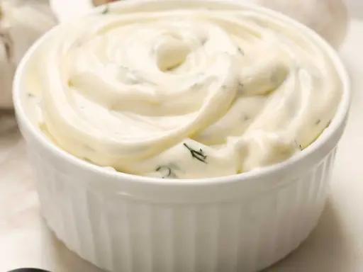 Un bol blanc rempli de sauce césar crémeuse, parsemée d'herbes vertes. Parfait pour accompagner une salade.