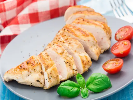 Un délicieux filet de poulet grillé, tranché et servi avec des tomates cerises et du basilic frais sur une assiette grise.