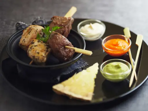 Brochettes de poulet et de bœuf, accompagnées de différentes sauces : mayonnaise, sauce tomate épicée et sauce verte.