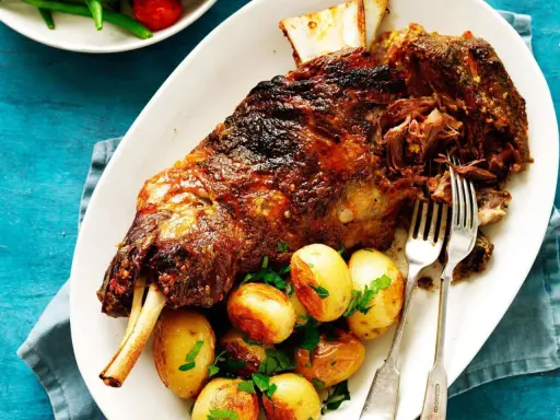 Épaule d'agneau rôtie, servie avec des pommes de terre et du persil. Le temps de cuisson de l'épaule d'agneau au barbecue Weber est parfait pour cette viande tendre.