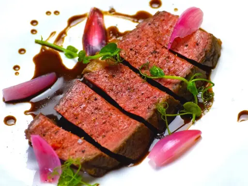 Une succulente entrecôte de bœuf, tranchée et nappée d'une sauce riche, accompagnée de jeunes pousses et d'oignons rouges marinés.