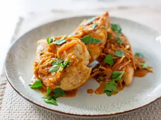 Trois escalopes de poulet nappées d'une sauce onctueuse aux oignons caramélisés et garnies de persil frais. Un plat savoureux et réconfortant.