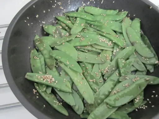 Pois gourmand croquants saupoudrés de graines de sésame dans une poêle.