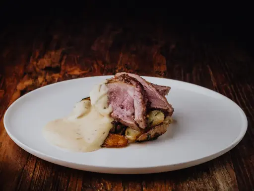 Tranches de gigot d'agneau rosées, nappées d'une sauce chasseur onctueuse, servies sur des pommes de terre rôties. Un délice pour les gourmands.