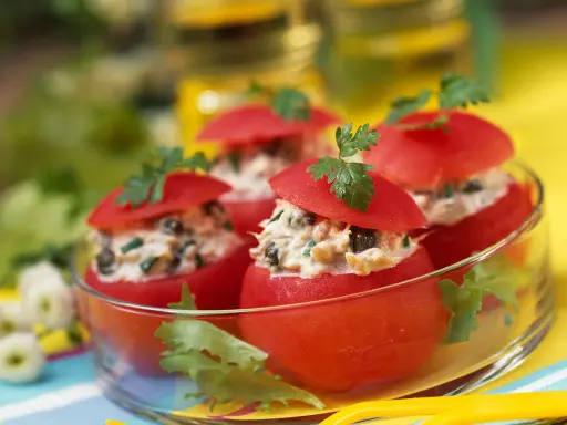 Tomates farcies froides aux légumes, garnies de persil frais, présentées dans un bol en verre. Un délice estival.