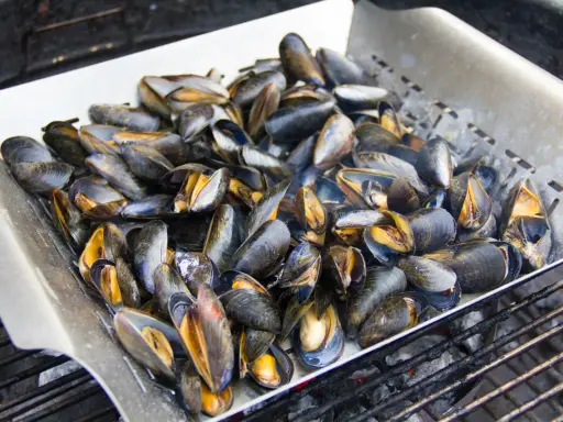 Un plateau de moules au barbecue, prêtes à être dégustées. Les coquilles sombres et orangées s'entrouvrent sous la chaleur des braises.