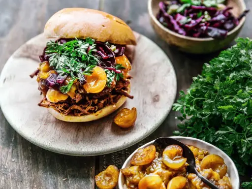 Un délicieux burger de pulled pork garni de fruits et de persil frais, accompagné d'une salade de chou rouge et de fruits confits.