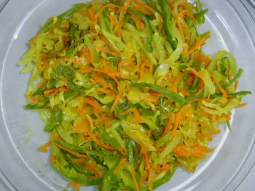Un plat coloré d'achard de légumes, mêlant carottes râpées, chou et poivrons verts, prêt à être dégusté.