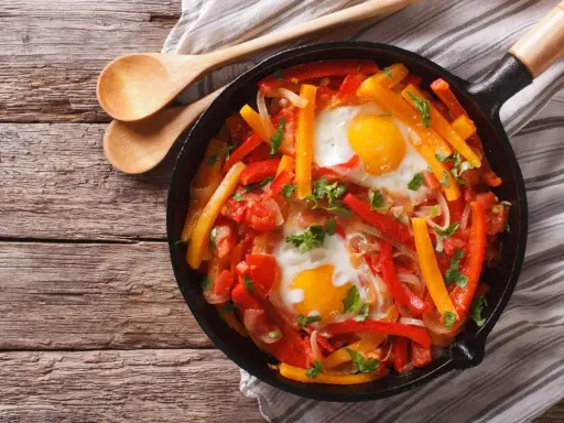 Poêlée de poivrons, tomates et œufs, une recette de piperade savoureuse, garnie de persil frais.