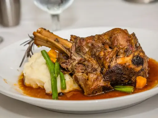 Une souris d'agneau braisée, servie avec une purée onctueuse, des haricots verts croquants et des dés de carottes, le tout nappé d'une sauce savoureuse.