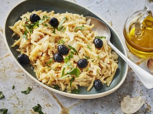 Un plat de bacalhau à brás, effiloché et garni d'olives noires et de persil frais. Une touche d'huile d'olive et d'ail est visible à côté.