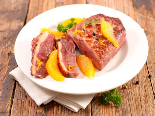 Magret de canard tranché, garni d'orange et de romarin, prêt à être dégusté. Une excellente recette plancha pour un repas savoureux.