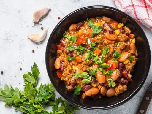 Un bol de chili sin carne, garni de persil frais, avec des haricots rouges, du maïs et des poivrons. Parfait pour un repas réconfortant.