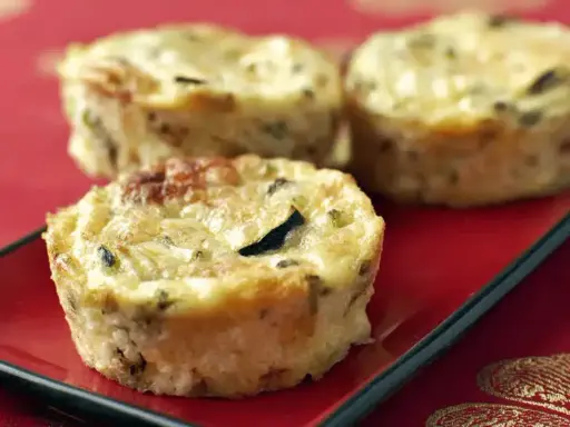 Trois petits flans de courgettes dorés et appétissants sur une assiette rouge, parfaits pour un repas léger.