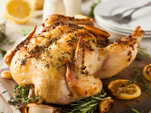 Un délicieux poulet rôti, doré et parfumé aux herbes, est servi sur une planche en bois avec des quartiers de citron et de l'ail rôti.