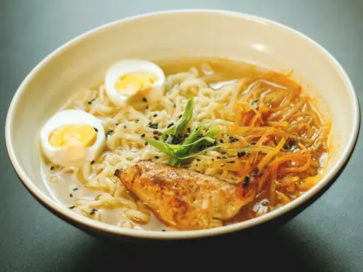 Un bol de ramen poulet avec nouilles, œuf dur, poulet grillé, julienne de carottes et oignons verts. Une recette réconfortante.