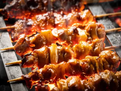 Brochettes de bœuf et fromage grillées sur des braises ardentes, dégageant une fumée alléchante.
