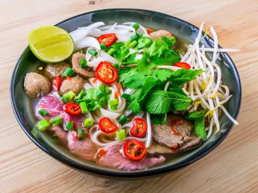 Un bol de soupe pho savoureux avec du bœuf, des boulettes, des nouilles, des herbes fraîches, des piments et un quartier de citron vert.