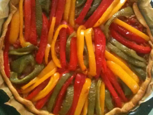 Tarte aux poivrons colorés, un délice visuel et gustatif. Les lanières de poivrons rouges, jaunes et verts forment un motif rayonnant sur la pâte dorée.