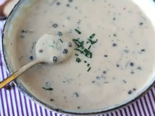 Une cuillère dorée plonge dans une onctueuse sauce au poivre, garnie de ciboulette fraîche.