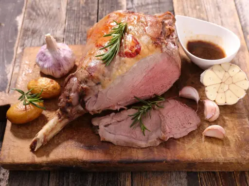 Gigot d'agneau rôti, servi avec des pommes de terre, de l'ail et une sauce. Une recette gastronomique qui met l'eau à la bouche.