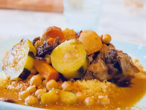 Un plat généreux de couscous algérien, garni de légumes tendres, de pois chiches et de morceaux de viande savoureux, le tout nappé d'une sauce parfumée.