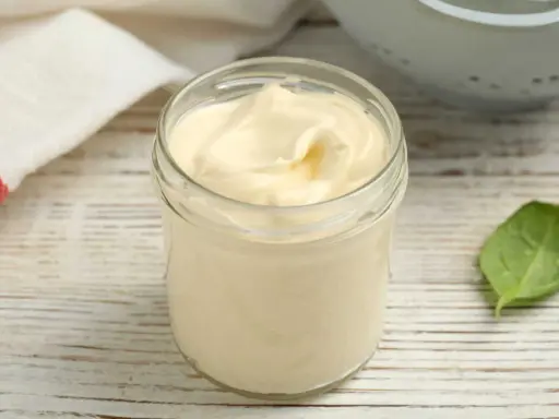 Un pot de mayonnaise sans huile, crémeuse et onctueuse, sur une table en bois. Une feuille verte à côté.