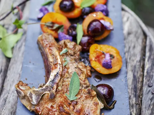 Délicieuse côte de veau barbecue, servie avec des abricots rôtis et des cerises, garnie de sauge fraîche.