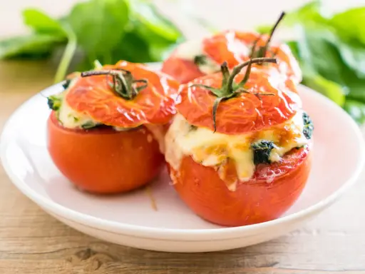 Trois tomates farcies au fromage fondant et aux herbes, servies sur une assiette blanche.