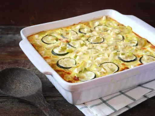 Un gratin de courgettes à l'ancienne, doré et crémeux, garni de rondelles de courgettes et de poireaux, prêt à être dégusté.