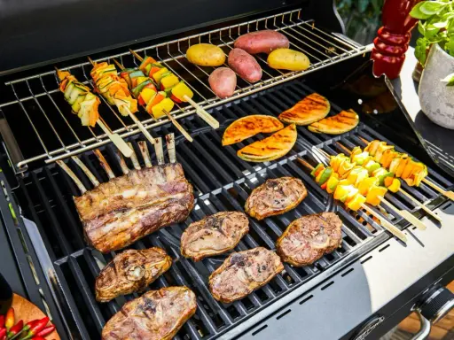 Côtelettes d'agneau, brochettes de légumes et pommes de terre sur un barbecue. La température du barbecue est parfaite pour une cuisson savoureuse.