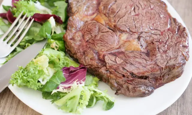 Une belle côte de bœuf juteuse, prête à être dégustée, accompagnée d'une salade fraîche. Parfait pour préparer un repas savoureux.