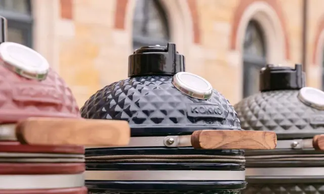 Trois barbecues kamado de couleurs différentes, prêts pour un avis. Le noir est au centre, le rouge à gauche, le gris à droite.
