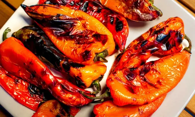 Poivrons rouges et orangés grillés au barbecue, légèrement noircis par la cuisson, sur une assiette blanche.