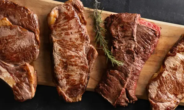 Quatre pièces de viande de saison octobre, grillées à la perfection, sur une planche en bois avec des herbes et du sel.