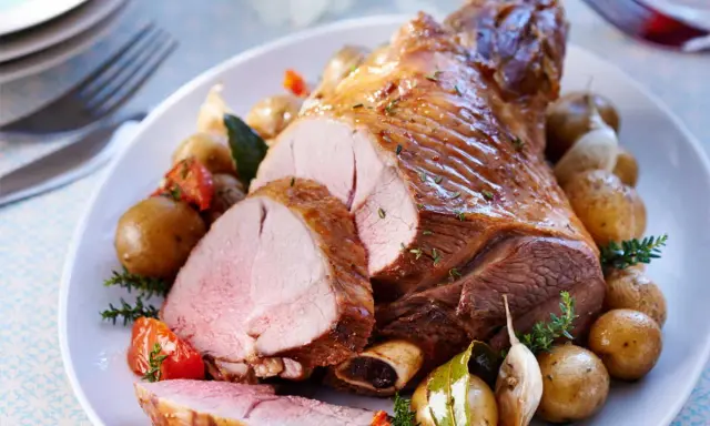 Un gigot d'agneau rôti, tranché, servi avec des pommes de terre nouvelles, tomates et ail. Parfait pour savoir que faire avec des morceaux de gigot d'agneau.