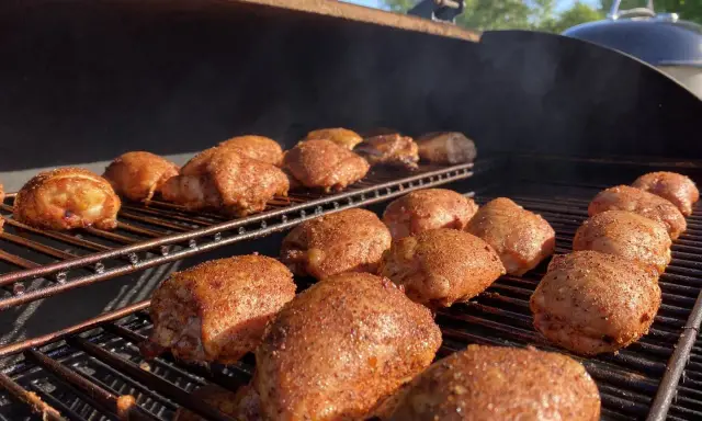 De nombreuses cuisses de poulet désossées, assaisonnées et grillées, fument sur un barbecue par une journée ensoleillée.