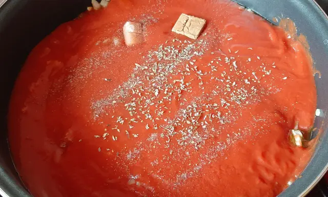 Sauce tomate maison mijote dans une poêle, agrémentée d'herbes et d'un cube de bouillon.