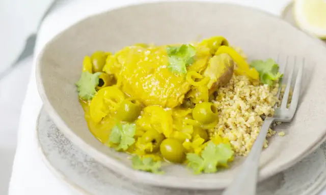 Un plat de tajine poulet citron, garni d'olives vertes et de coriandre fraîche, servi avec du couscous.