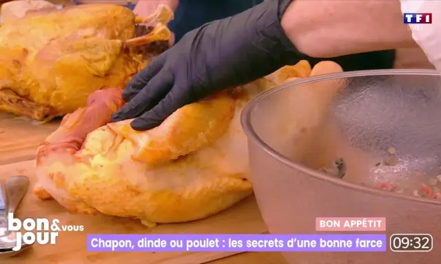 Main d'un cuisinier en gant noir préparant une farce poulet avec abats. Un chapon doré est à côté.