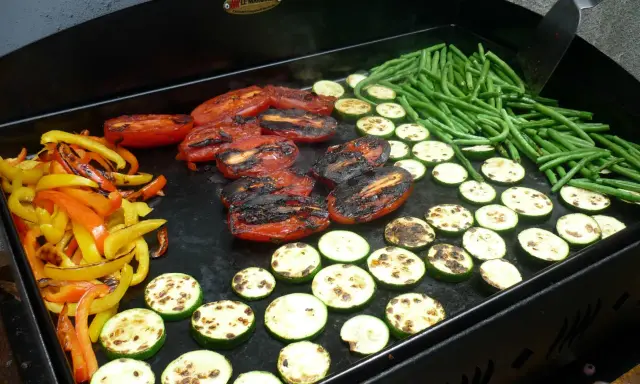 Légumes variés (poivrons, courgettes, tomates, haricots verts) en cours de cuisson sur une plancha. Le temps de cuisson des légumes à la plancha est idéal pour un repas sain et savoureux.
