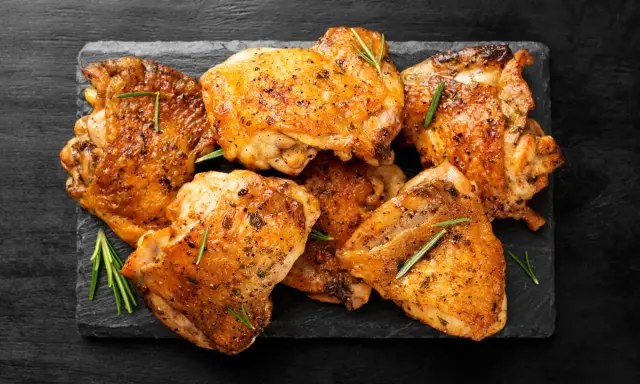 Pile de haut de cuisse de poulet grillé, assaisonné d'herbes et de poivre, sur une ardoise noire.